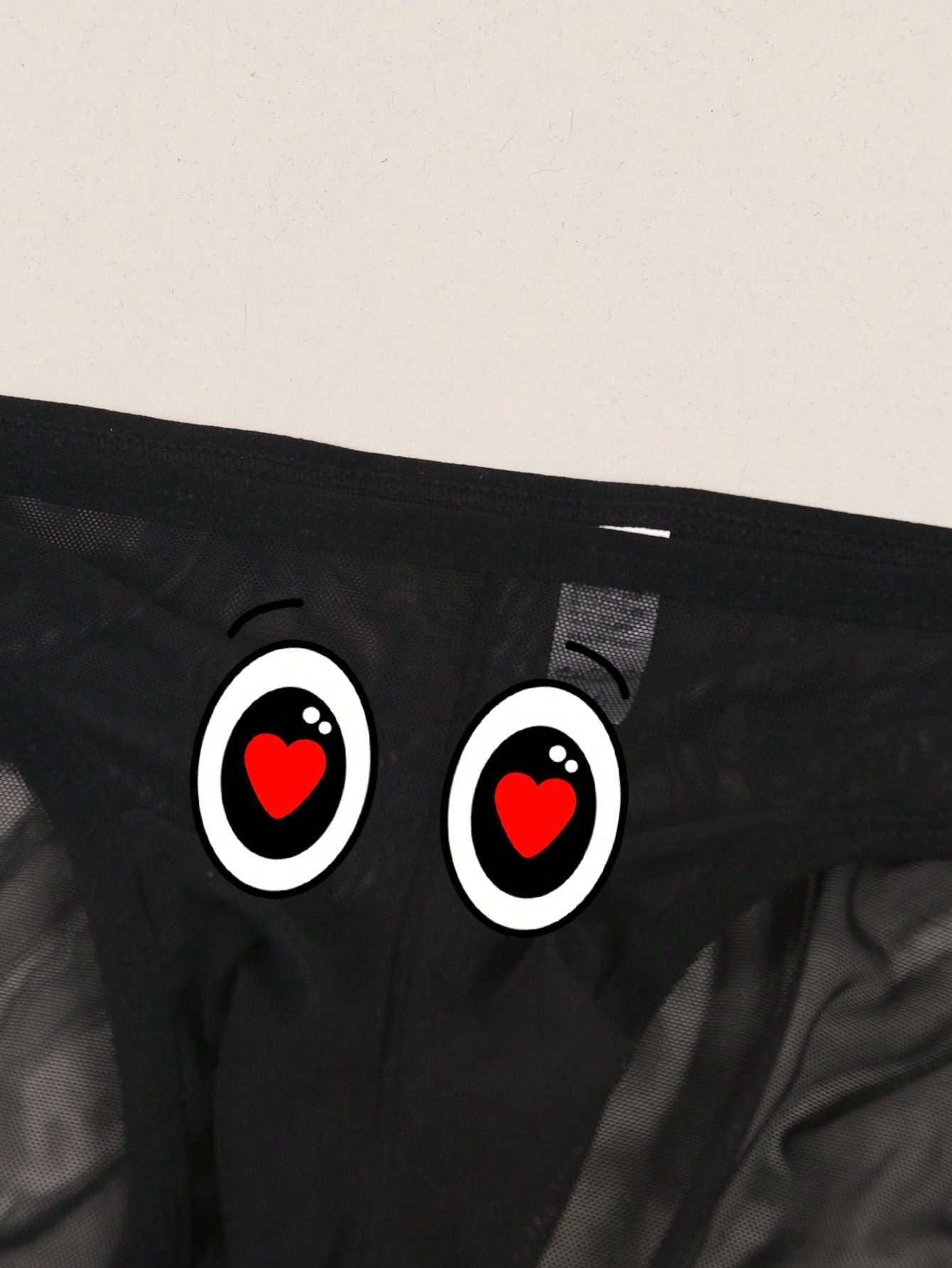 Men's black semi-sheer mesh thong with heart eye print pattern, low-rise cut, and breathable knitted fabric.
