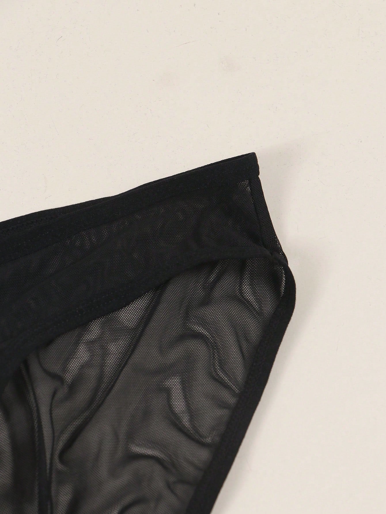 Men's black semi-sheer mesh thong with heart eye print pattern, low-rise cut, and breathable knitted fabric.