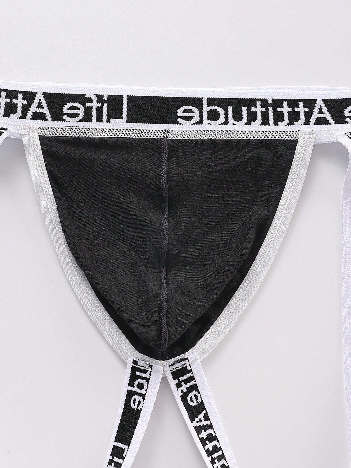 Men's black low-rise thong with letter print, hollow out tape design, and medium-stretch knitted fabric.