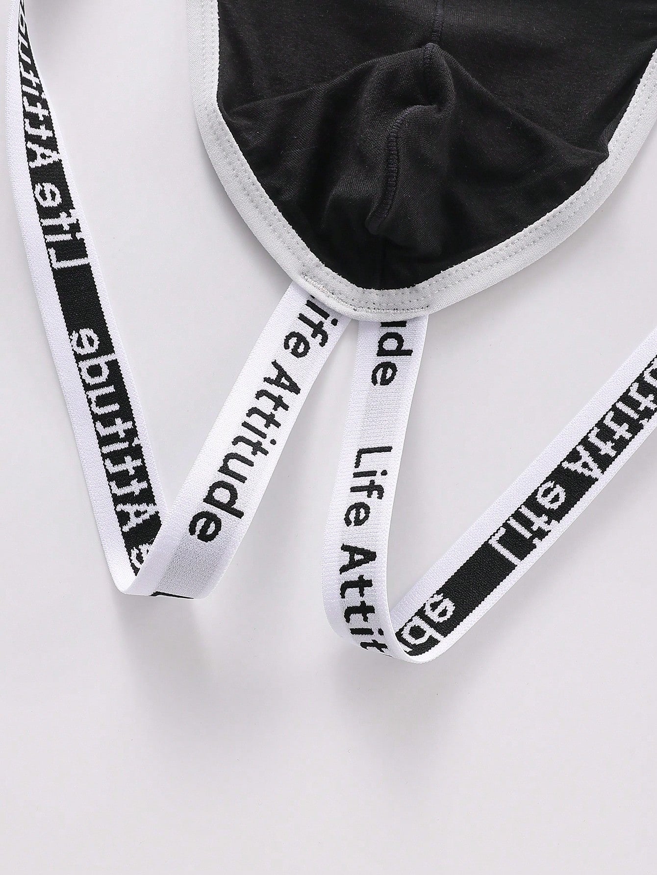 Men's black low-rise thong with letter print, hollow out tape design, and medium-stretch knitted fabric.