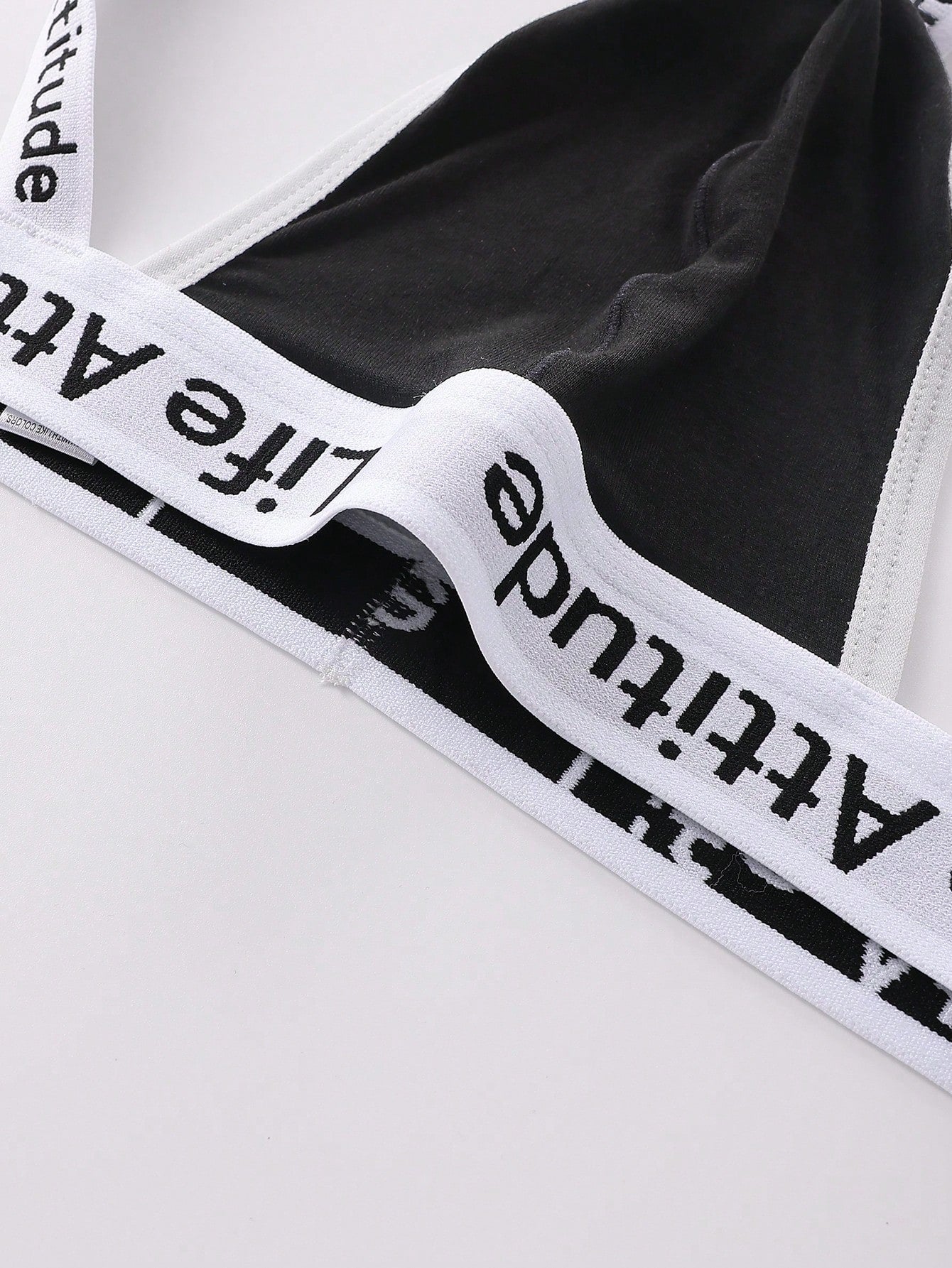 Men's black low-rise thong with letter print, hollow out tape design, and medium-stretch knitted fabric.
