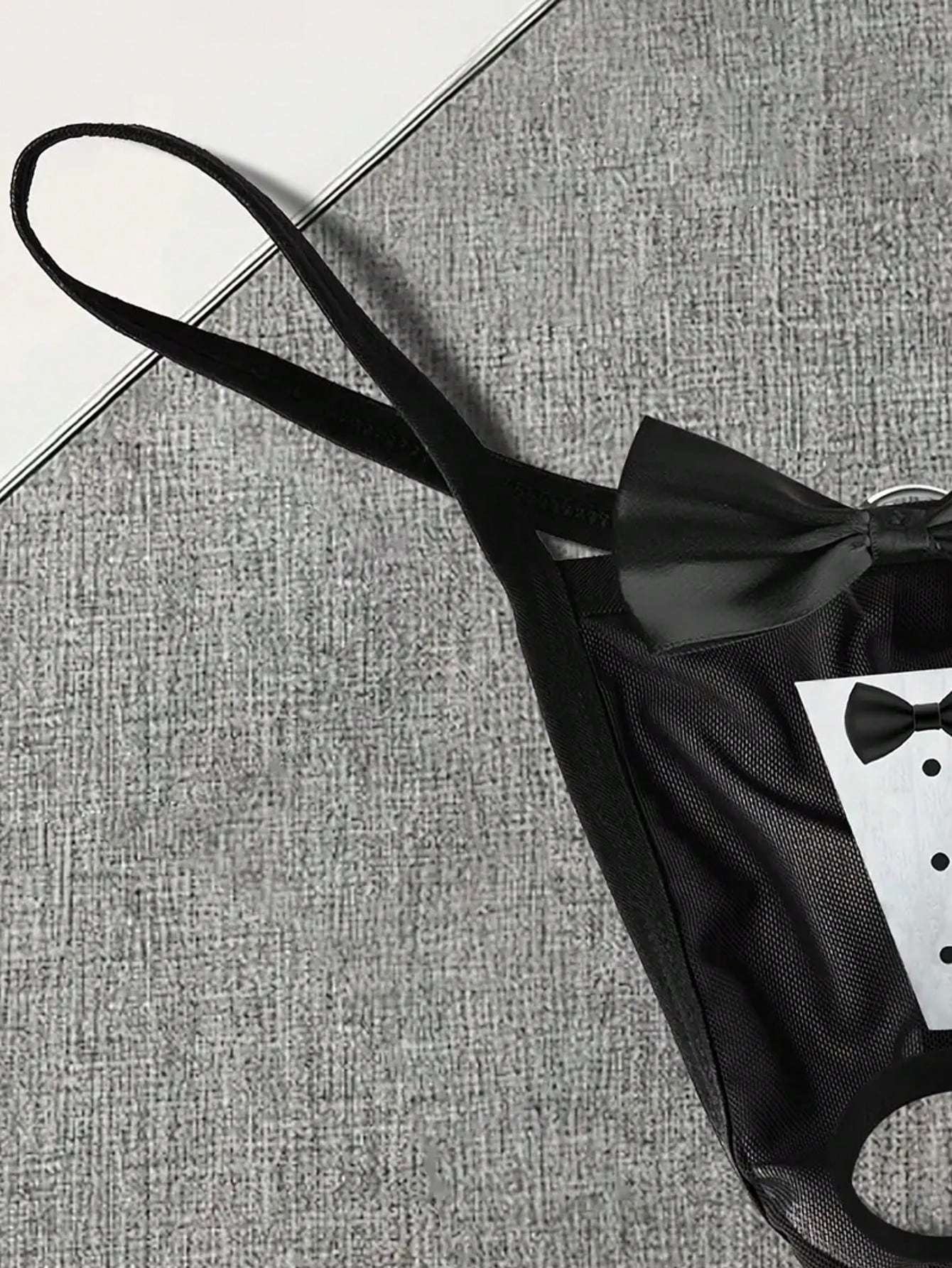 Men's black sheer mesh thong underwear with Halloween bow print pattern, bow decor, and cut-out details