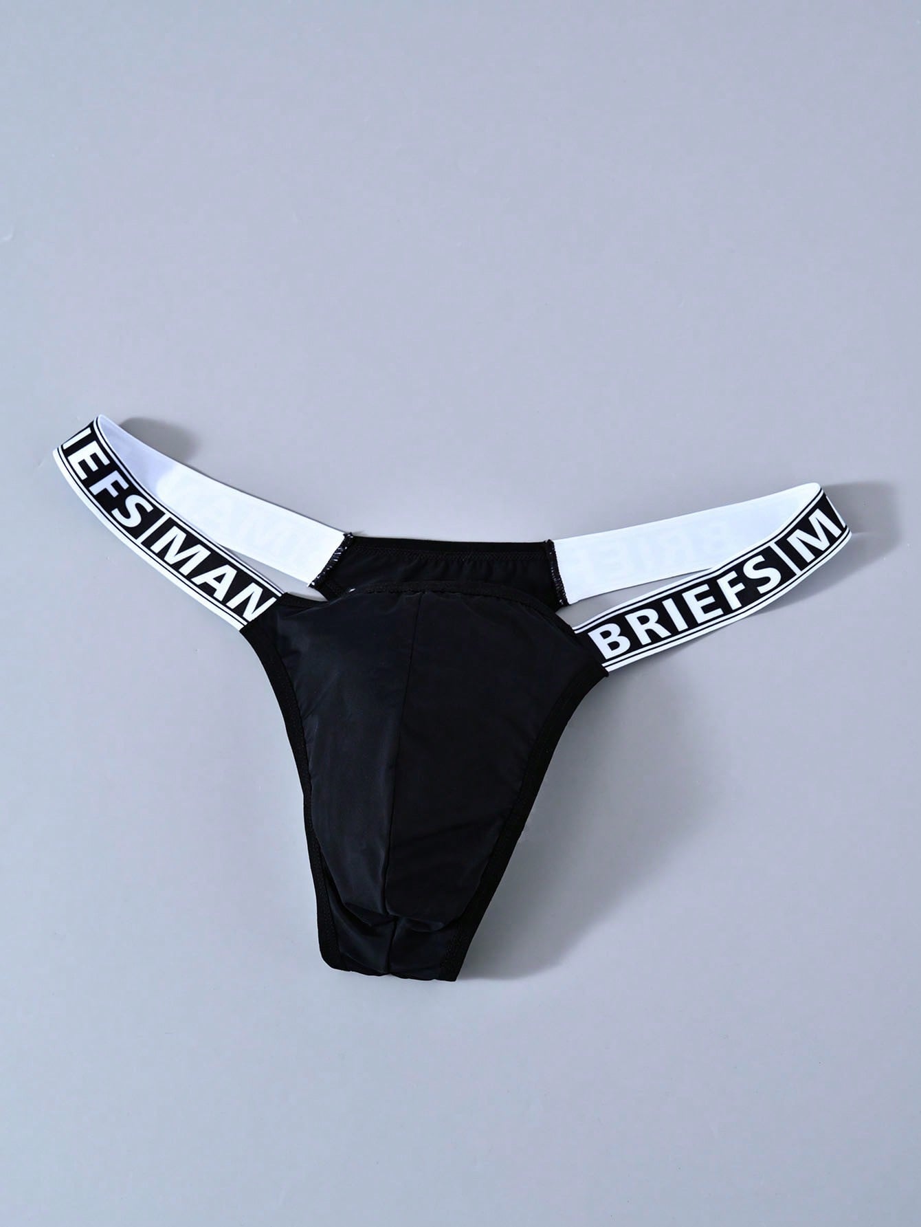 Men's solid color thong underwear with a letter waistband, textured pattern, tape detail, and mid-rise fit