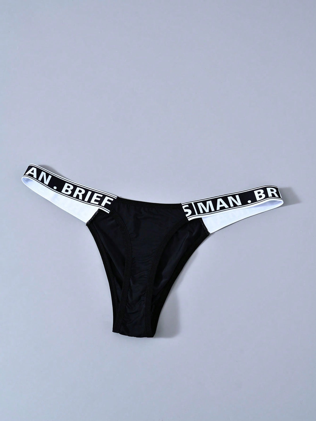 Men's solid color thong underwear with a letter waistband, textured pattern, tape detail, and mid-rise fit