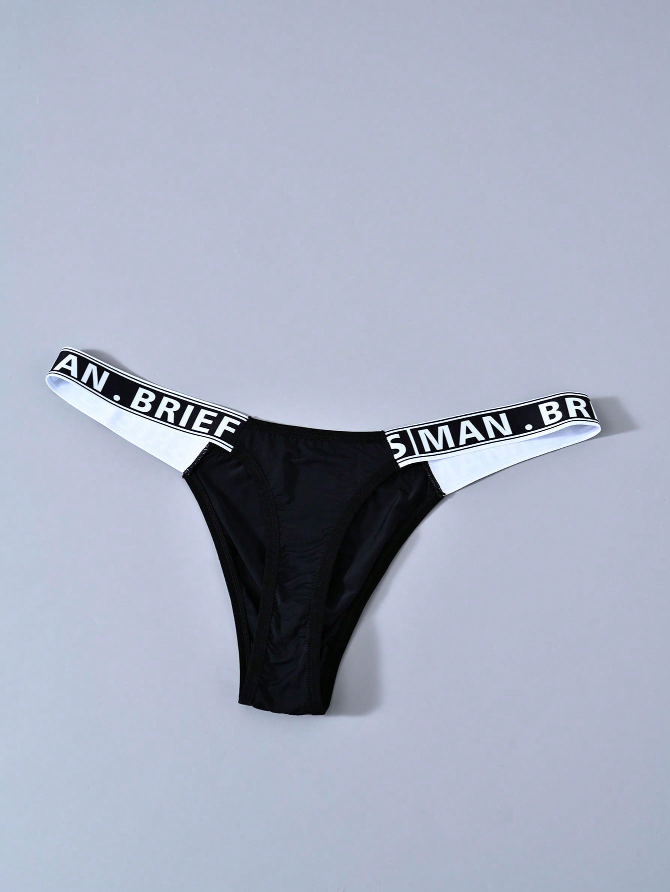 Men's solid color thong underwear with a letter waistband, textured pattern, tape detail, and mid-rise fit