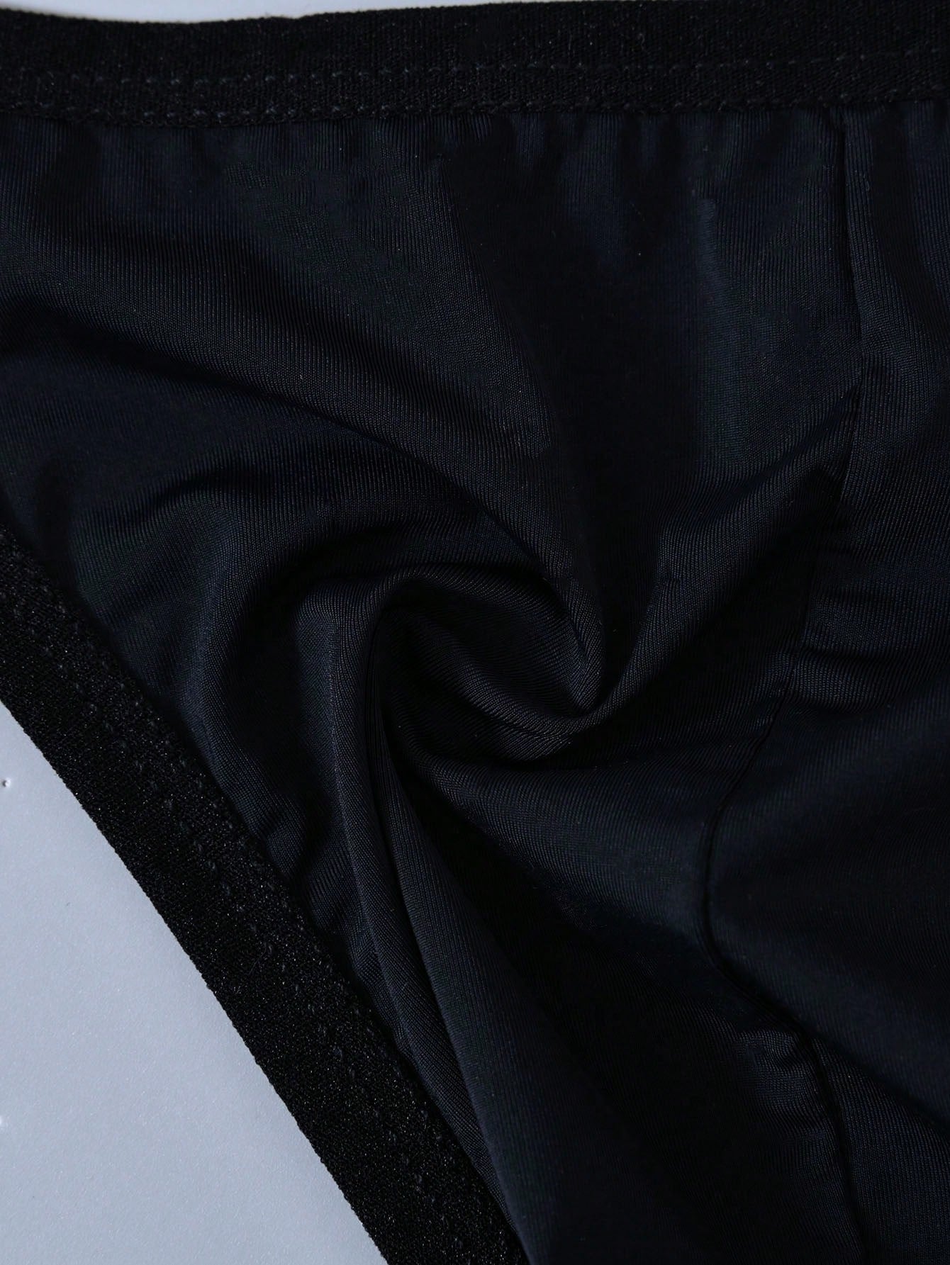 Men's solid color thong underwear with a letter waistband, textured pattern, tape detail, and mid-rise fit