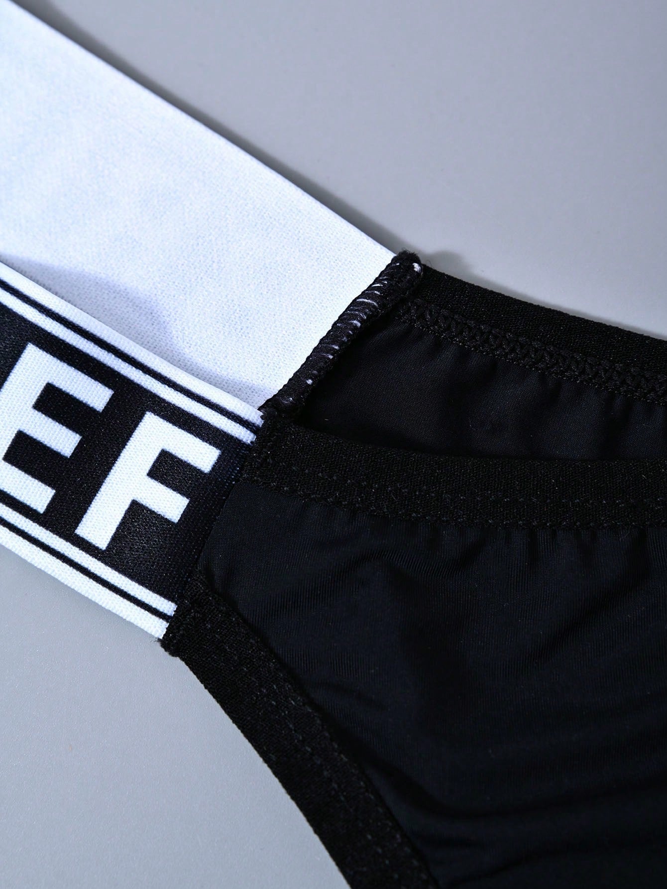 Men's solid color thong underwear with a letter waistband, textured pattern, tape detail, and mid-rise fit
