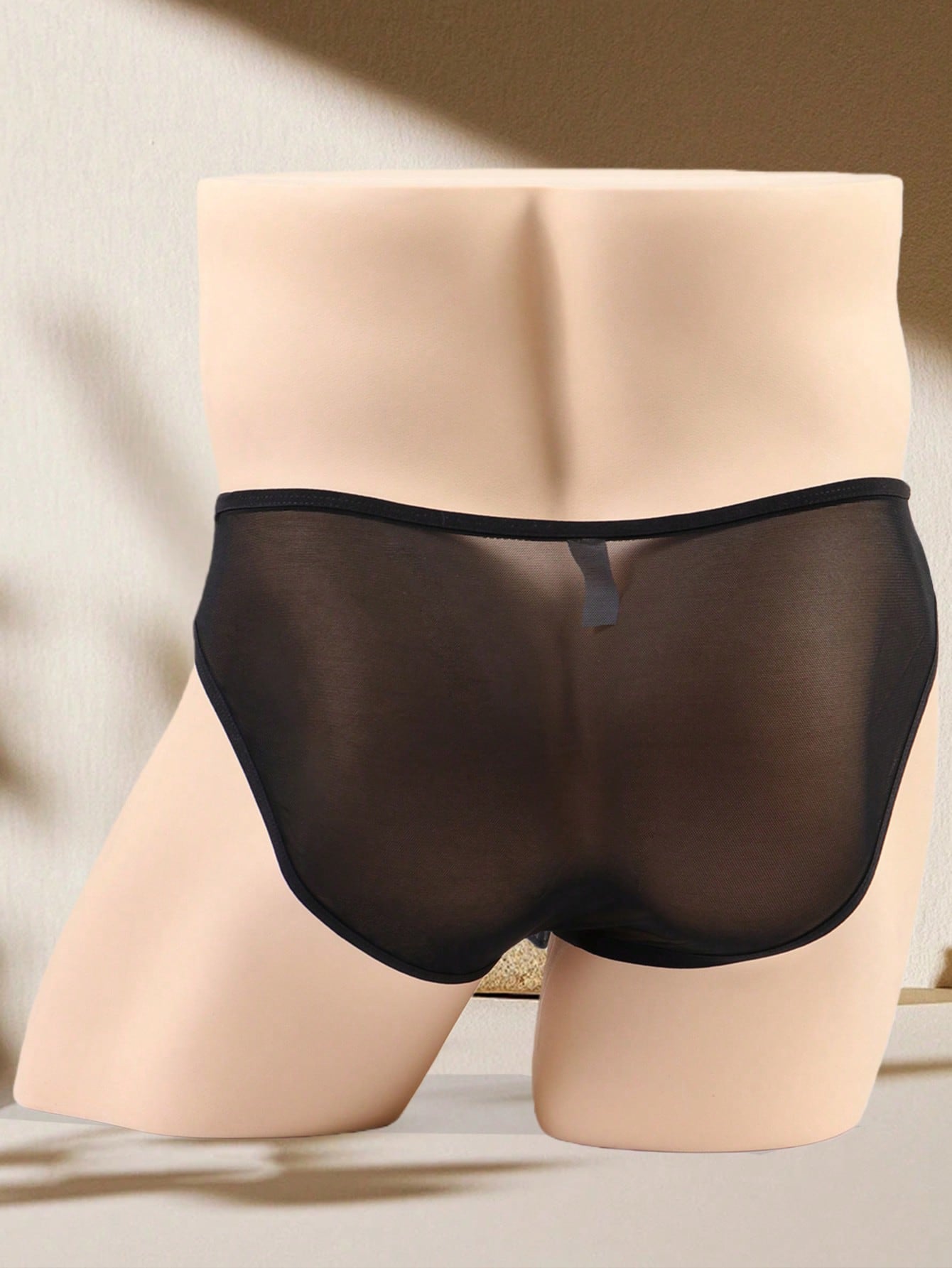 Men's black semi-sheer mesh thong with heart eye print pattern, low-rise cut, and breathable knitted fabric.