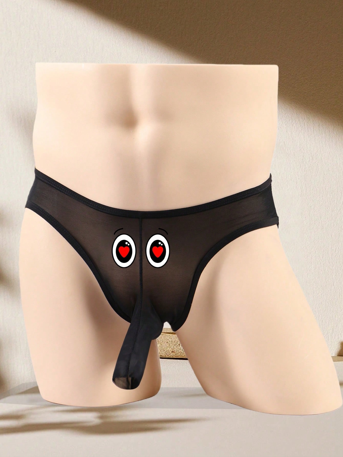 Men's black semi-sheer mesh thong with heart eye print pattern, low-rise cut, and breathable knitted fabric.