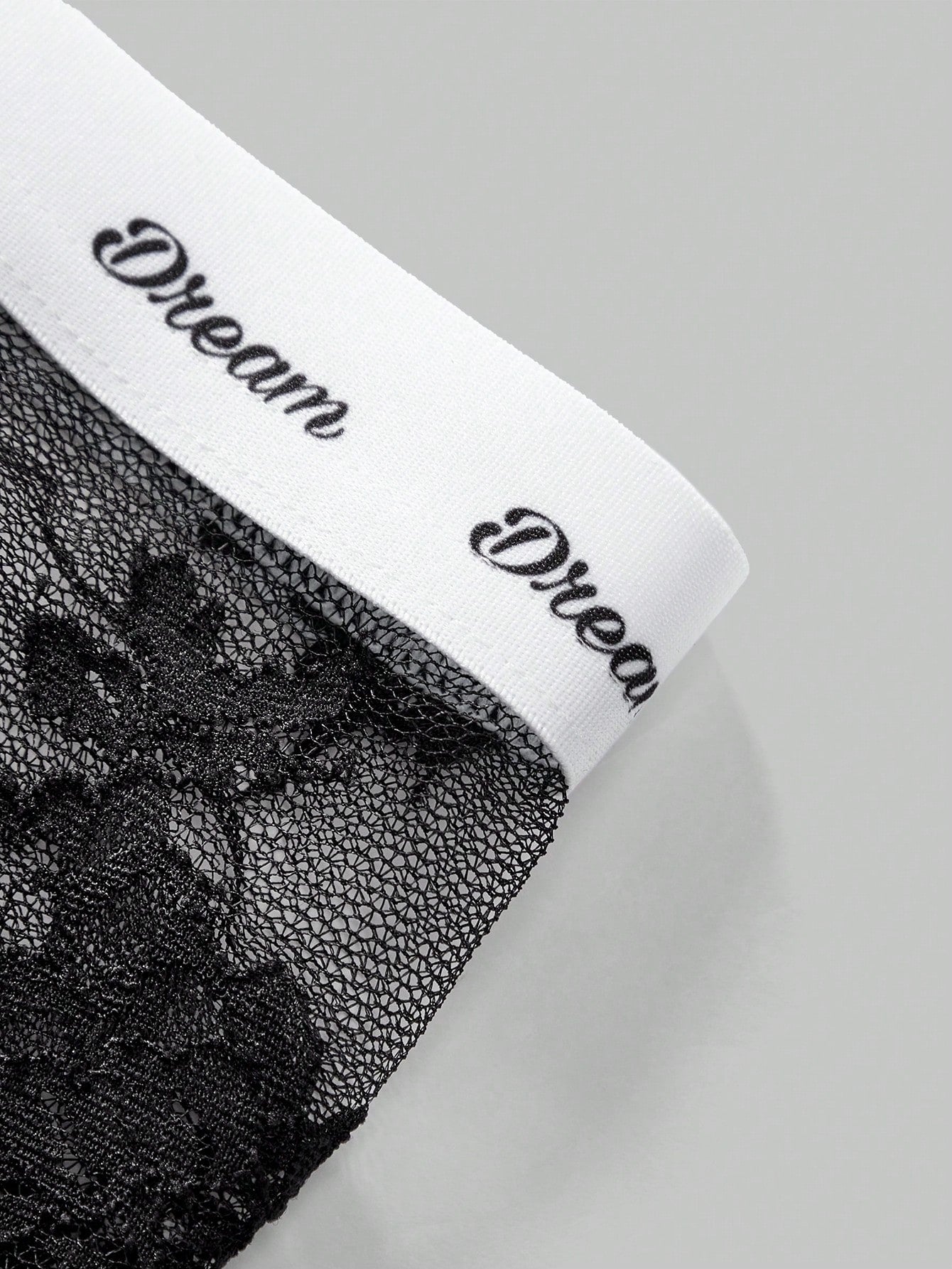 Men's black and white lace trim briefs with tape details and letter and plant pattern, shown as a short regular-fit underwear style.