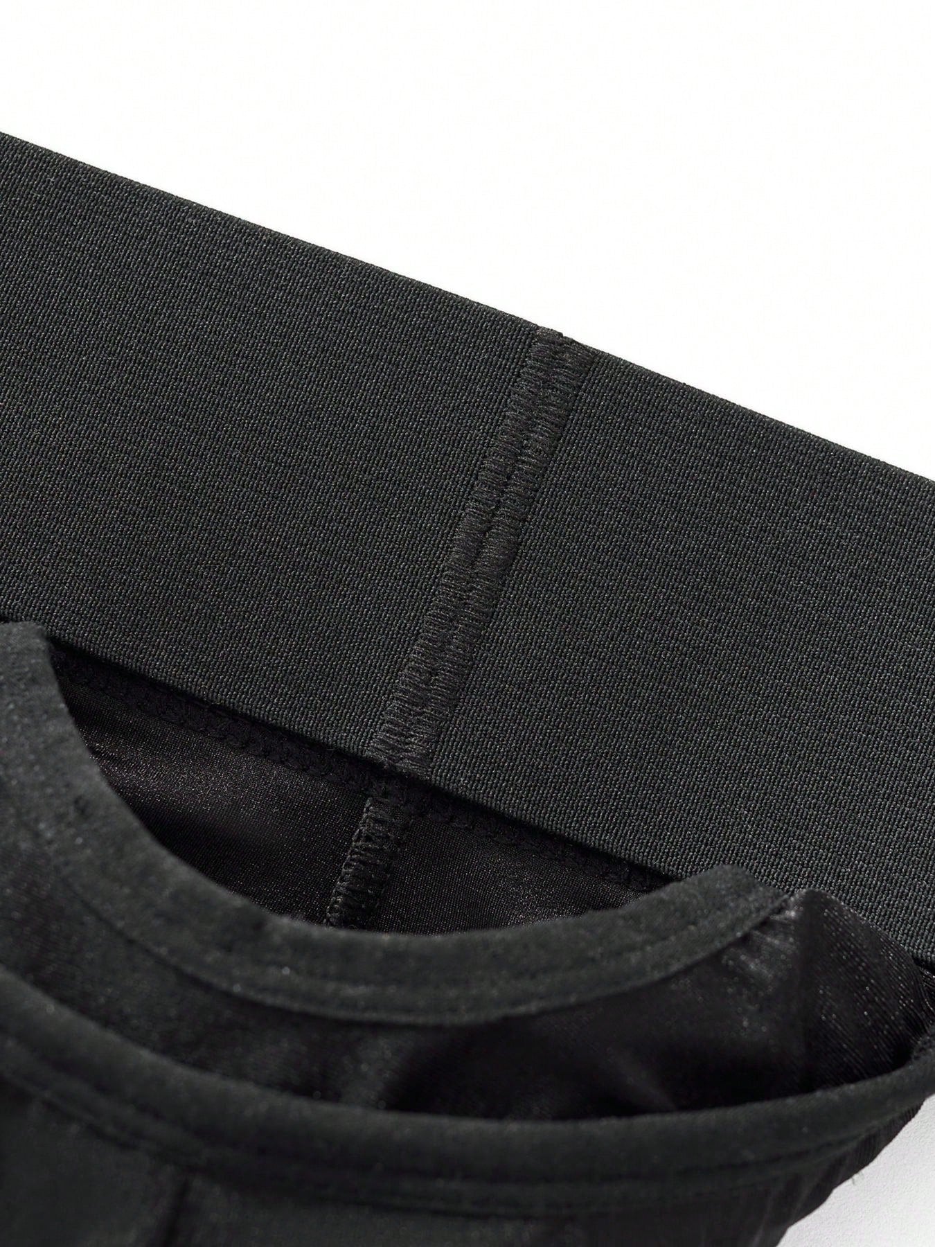 Men's black low-rise thong underwear with wide waistband and letter pattern, made from medium-stretch fabric.