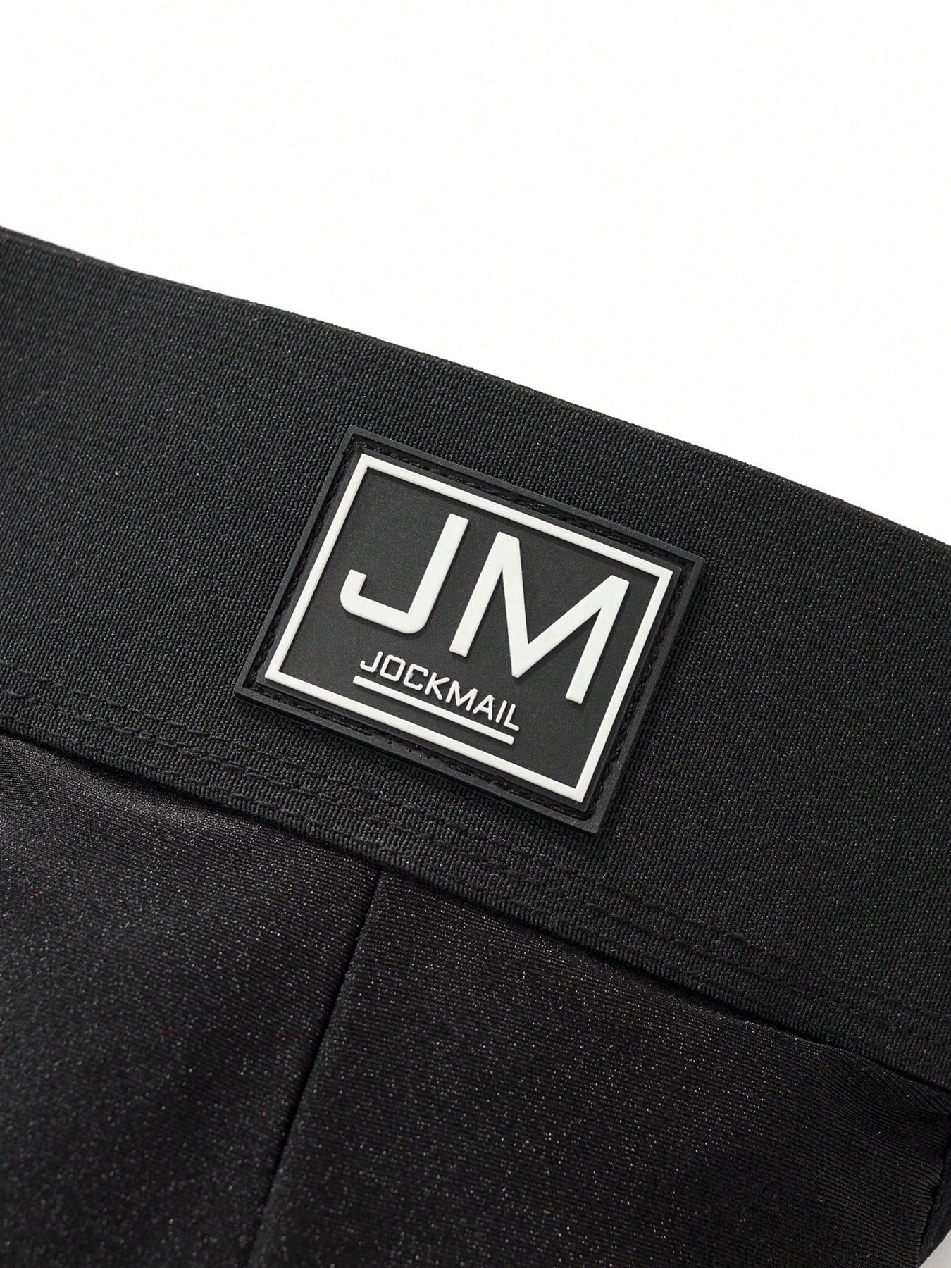 Men's black low-rise thong underwear with wide waistband and letter pattern, made from medium-stretch fabric.