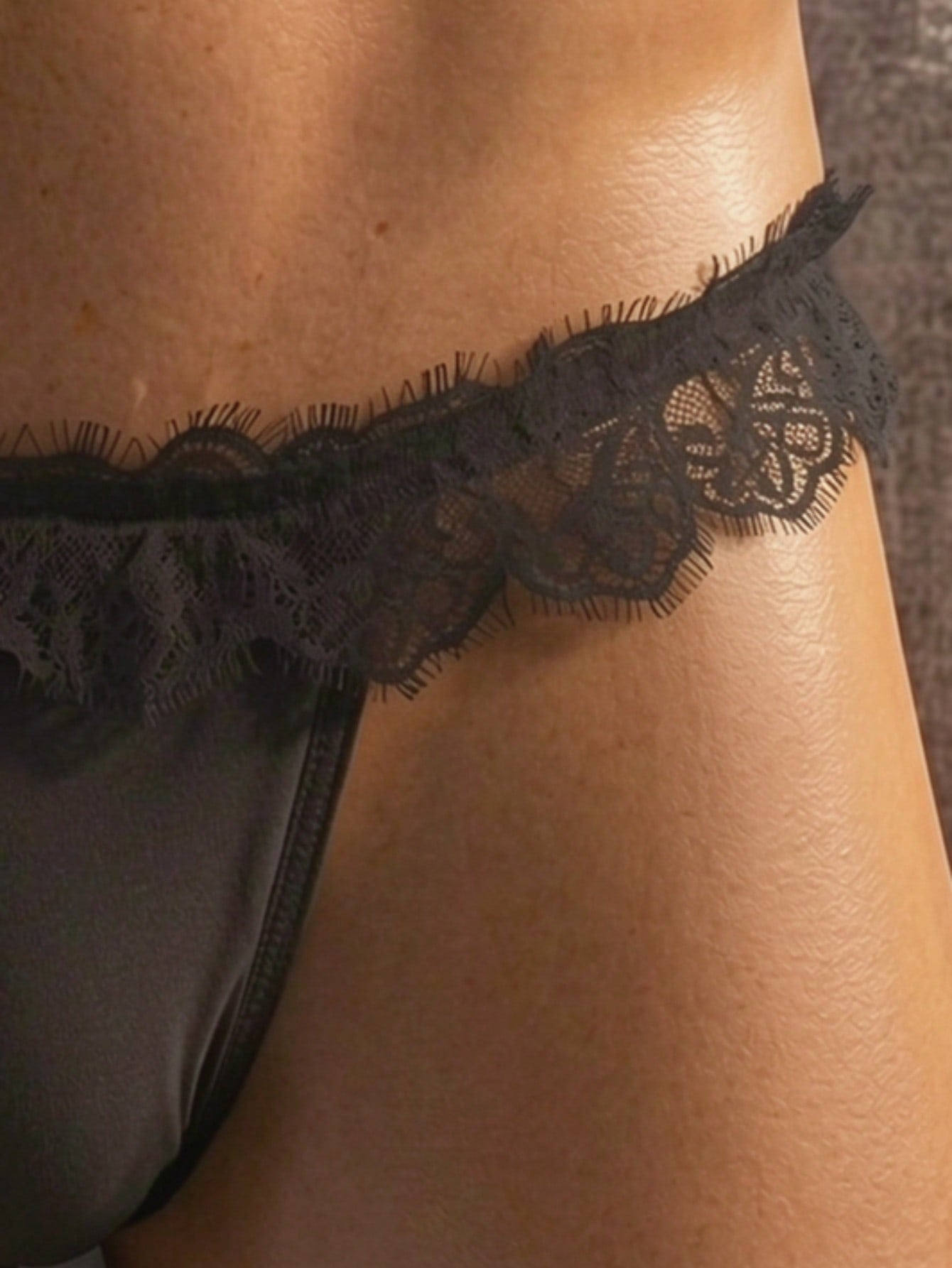 Men's black low-rise thong underwear with lace mesh styling, contrast lace, and bow detail